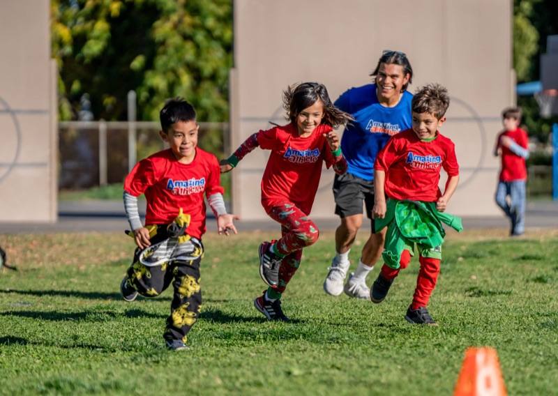 An Amazing Athletes coach running across a school field alongside three laughing children