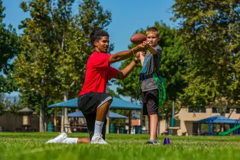 An Amazing Athletes coach kneeling to hold a football while a boy lines up a kick