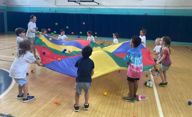 Children lifting a rainbow parachute together in a school gym