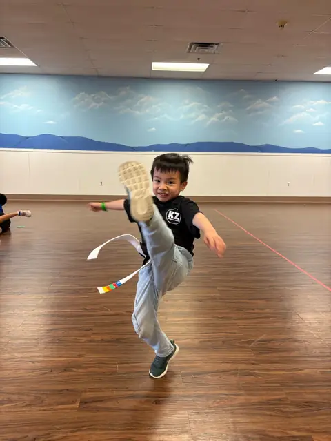 A boy in a Karate Zoo shirt in the middle of a high kick