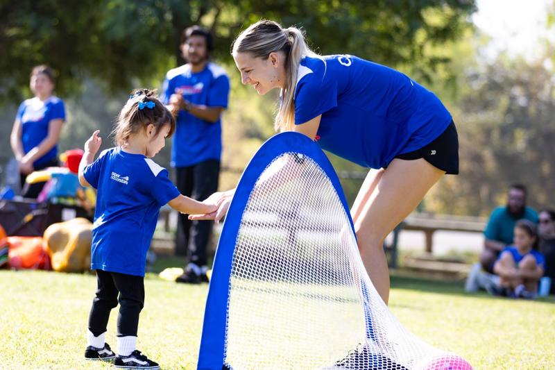 A Soccer Stars coach leaning over a pop-up goal to high-five a toddler
